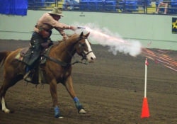 Man riding a horse in an arena while shooting at a target. The vibe is exciting and competitive.