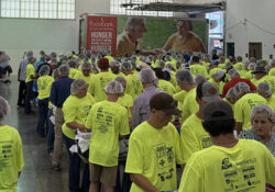 Kids in bright yellow shirts stand in a building with a Feeding Missouri trucki in the backgrounds. The enviorment suggests food packing.