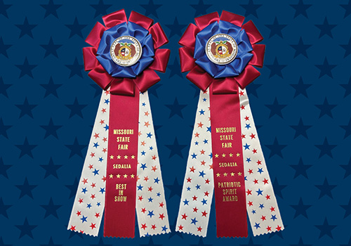 Two festive ribbon rosettes with blue, red and white colors feature gold text: "Missouri State Fair, Sedalia," on a star-patterned background.