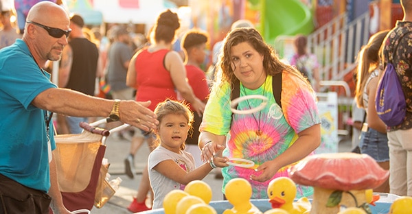 A woman and girl playing ring toss at the fair carnival