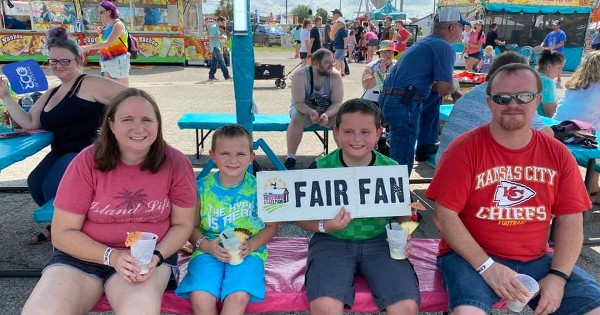 A family at the fair with a young boy holding a sign that says fair fan