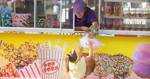 A concessionaire handing a young girl cotton candy