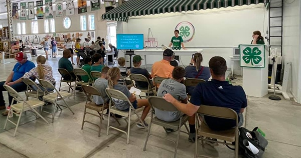 Attendees listening to a 4-H member speak at a podium