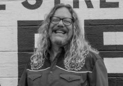 Ray Cardwell smiling and standing in front of a brick wall