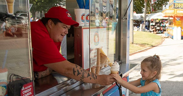 A smiling fair vendor handing an excited young girl an ice cream cone